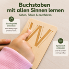 Kind fährt eine gravierte Holz-Buchstabenkarte mit dem Finger nach und lernt Buchstaben mit allen Sinnen