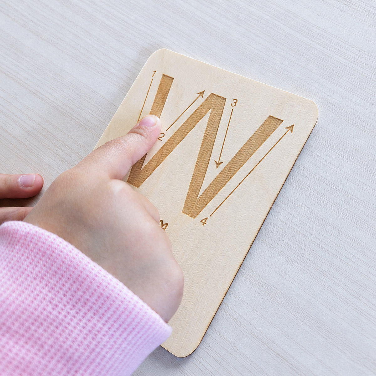 Kind fährt eine gravierte Holz-Buchstabenkarte mit dem Finger nach und lernt Buchstaben mit allen Sinnen