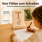 Kind übt erste Schreibbewegungen mit einer sensorischen Buchstabenkarte aus Holz und schreibt den Buchstaben T auf Papier