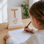 Kind übt erste Schreibbewegungen mit einer sensorischen Buchstabenkarte aus Holz und schreibt den Buchstaben T auf Papier